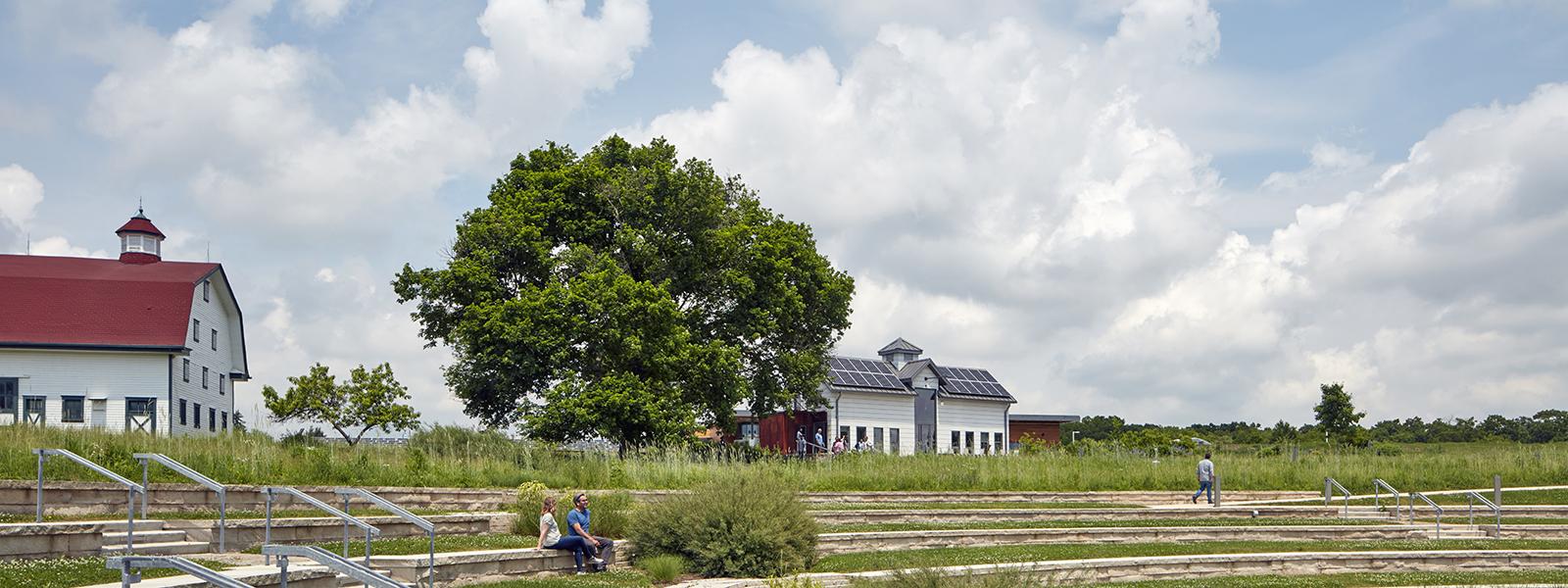 Photo of the tiered amphitheater at Chatham University's Eden Hall Farm featuring a white dairy barn and larger barn.